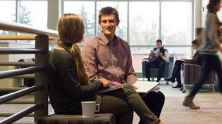 A male and female student talking on a bench